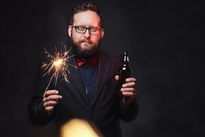 Fat male in eyeglasses dressed in a shirt with bow tie drinks craft beer from a bottle.