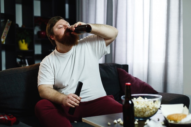 Free photo fat man drinks beer lying on the sofa