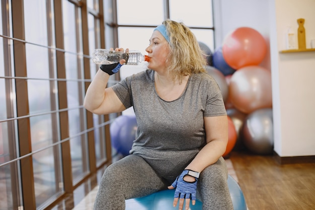 Fat woman dieting, fitness. Lady sitting on a fitball and driking a water.