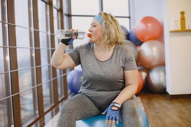 Толстая женщина на диете, фитнес. Дама сидит на фитболе и обдувает воду.