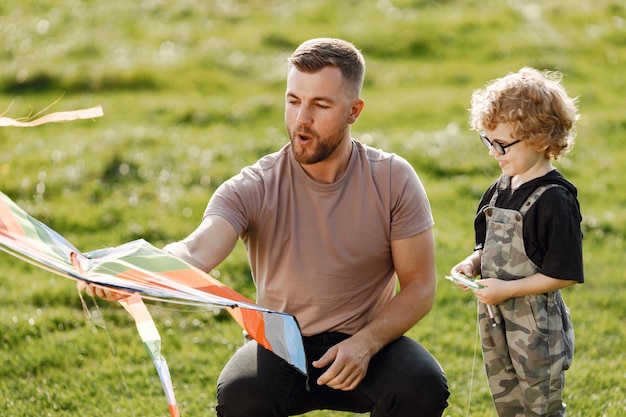 凧で遊んで、夏の公園の屋外で楽しんでいる父と息子カーリー幼児の男の子は眼鏡をかけています