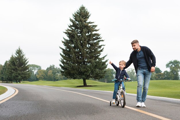Отец и ребенок играют в парке с велосипедом