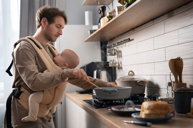 Foto gratuita padre che cucina mentre tiene in braccio il bambino medio