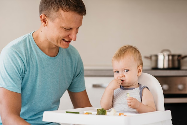 Free photo father and cute baby in highchair eating