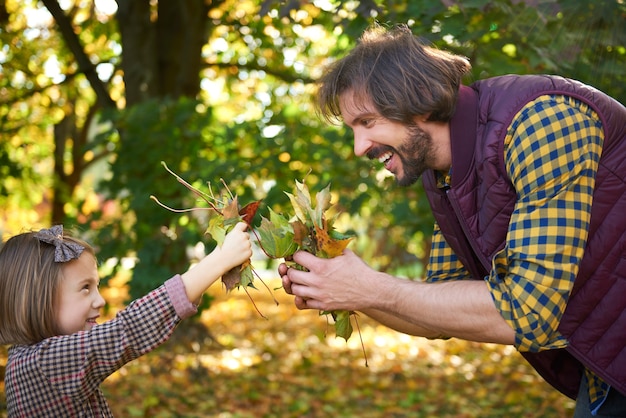 Отец и дочь собирают листья осенью