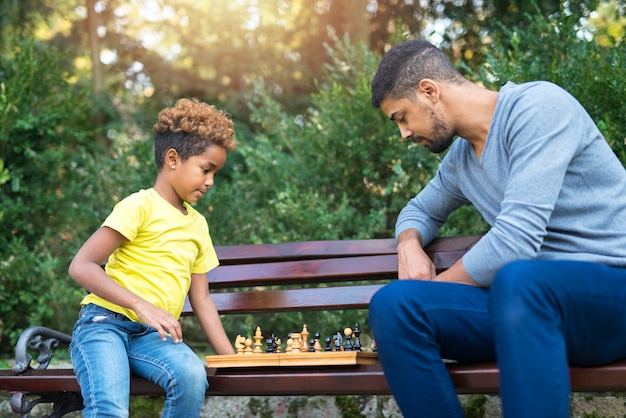Отец и дочь играют в шахматы в парке