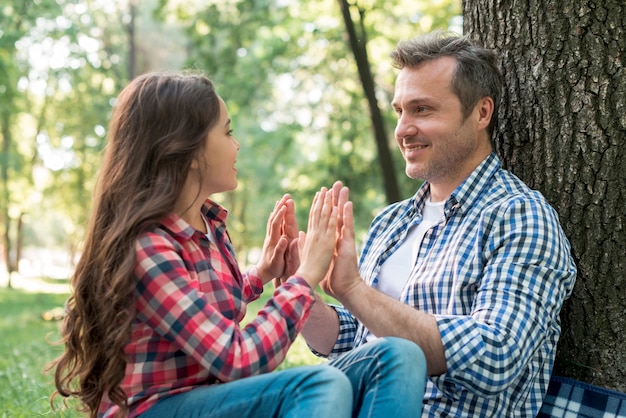 Free photo father and daughter playing pat-a-cake game during sitting in park