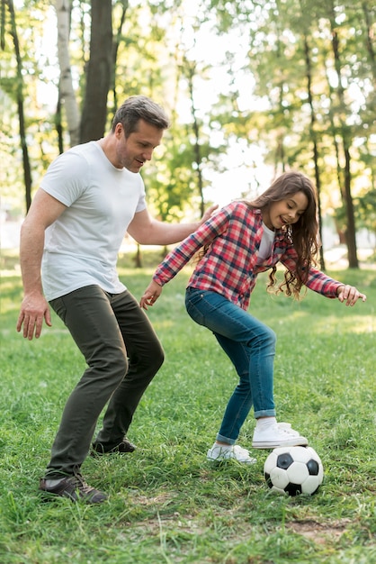 Отец и дочь играют в футбольный мяч в парке
