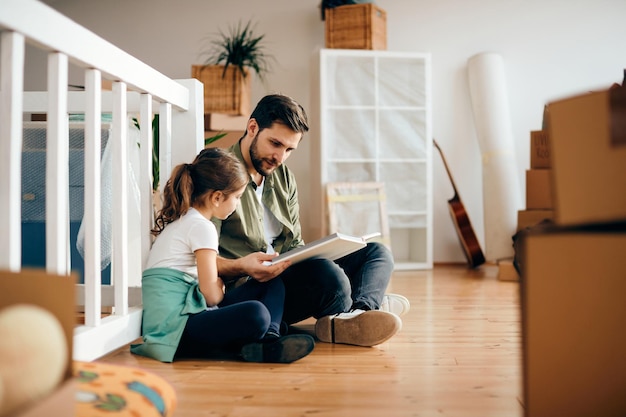 Отец и дочь читают книгу во время переезда в новую квартиру