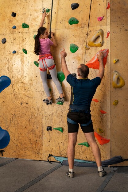 Free photo father and daughter rock climbing together indoors at the arena