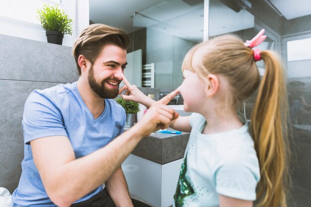 Father and daughter smearing cream on noses