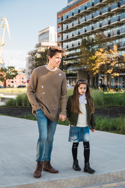 Father and daughter standing on pavement holding hands