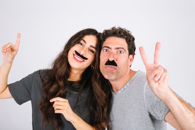 Father and daughter with artificial moustaches gesturing peace