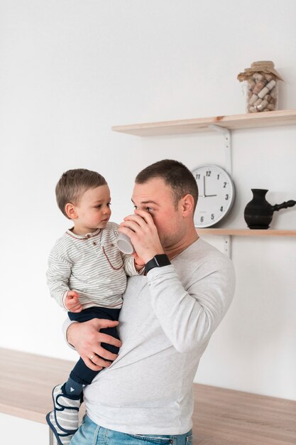 Father drinking from mug while holding baby