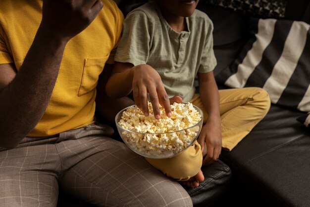 Father eating popcorn with son on the sofa at home