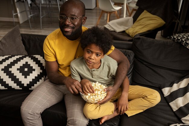 Father eating popcorn with son on the sofa at home