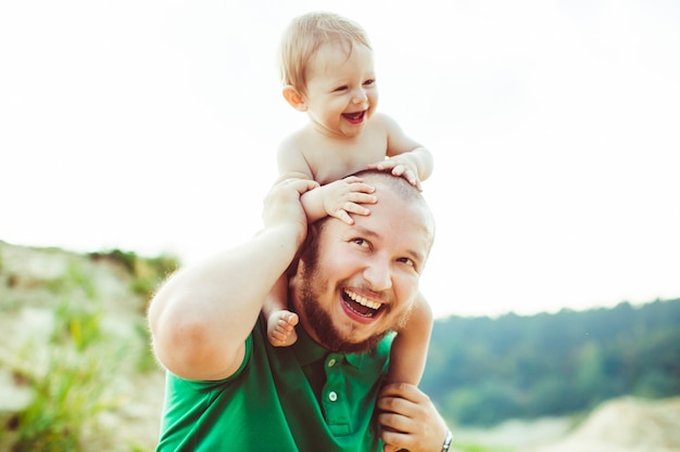 緑のシャツの父親は首に小さい息子を抱えている