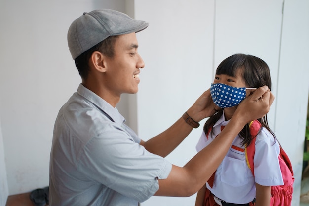 Father helping her daughter to wear a mask before going to school in the morning to prevent from a covid 19 virus