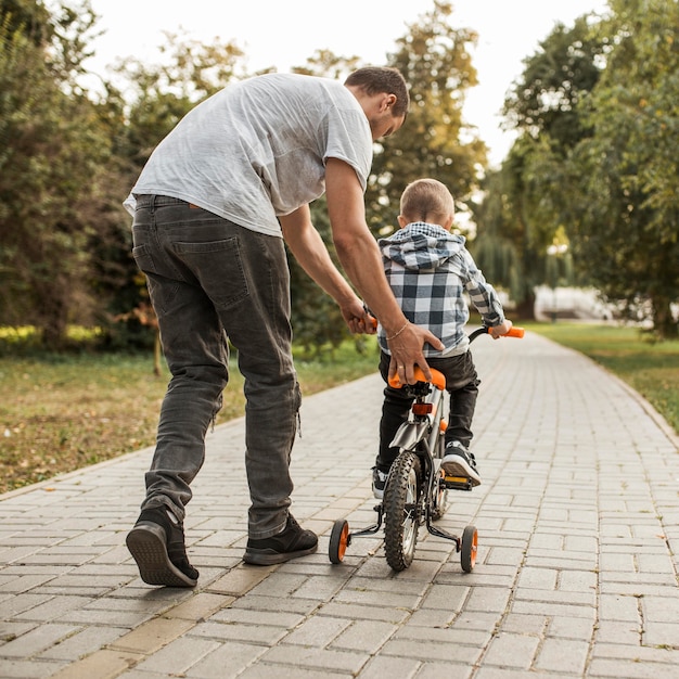 Отец помогает своему сыну ехать на велосипеде сзади выстрел