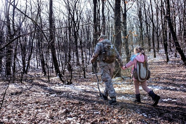 Отец и его дочь путешествуют по раннему зимнему лесу в камуфляжной походной одежде