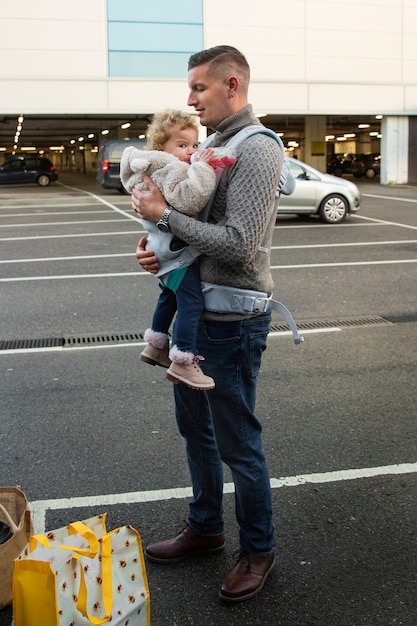 Free photo father holding baby in carrier full shot