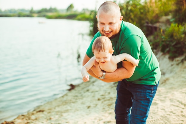 "Father holding baby standing on sand shore"