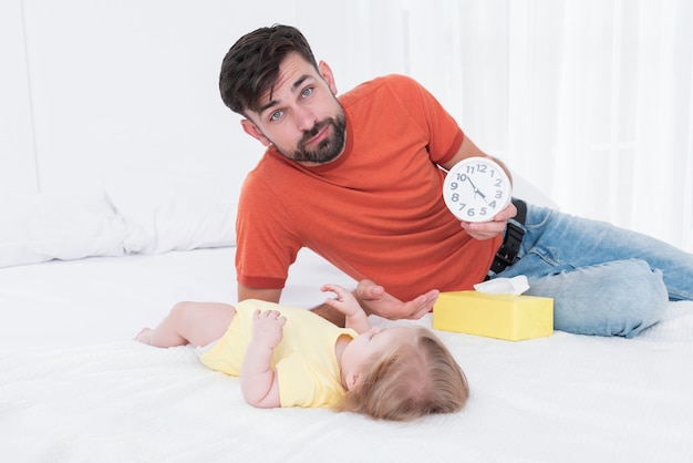 Отец держит часы рядом с ребенком в постели