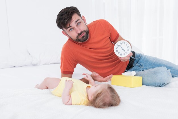 Father holding clock next to baby in bed