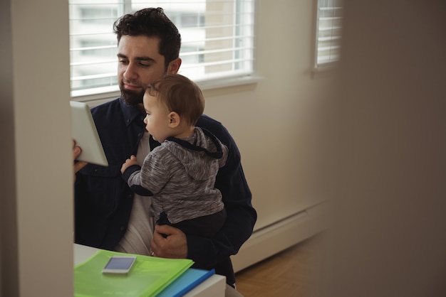 Father holding his baby while using digital tablet at desk