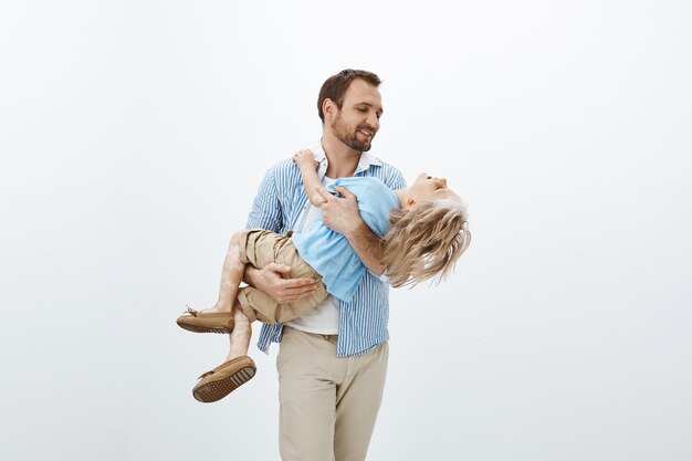 Father holding precious treasure in hands. Portrait of cute happy european dad in casual outfit carrying son in arms, smiling and looking at boy face