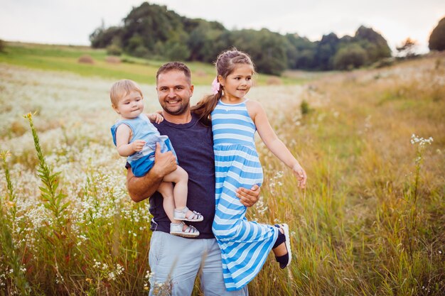 Father holds his children on the arms standing on the field 