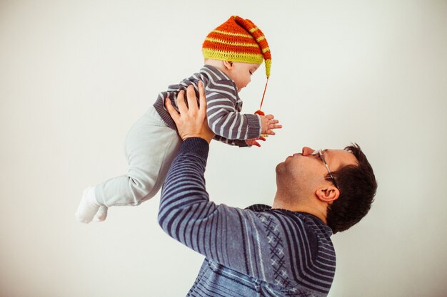 Father holds tender little son in stripped hat 