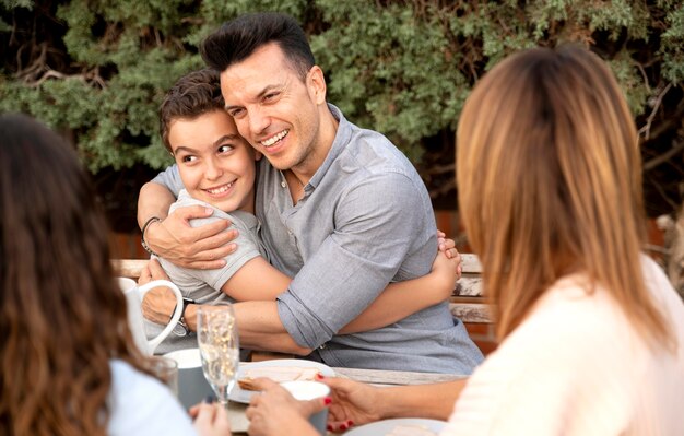 Padre che abbraccia suo figlio mentre pranza in famiglia all'aperto