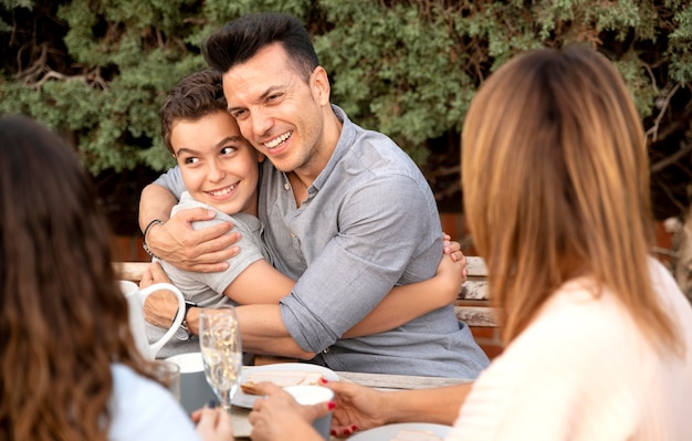 Отец обнимает сына во время семейного обеда на открытом воздухе