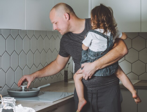 Отец готовит ужин на кухне с дочерью на руках, мужчина делает домашние дела
