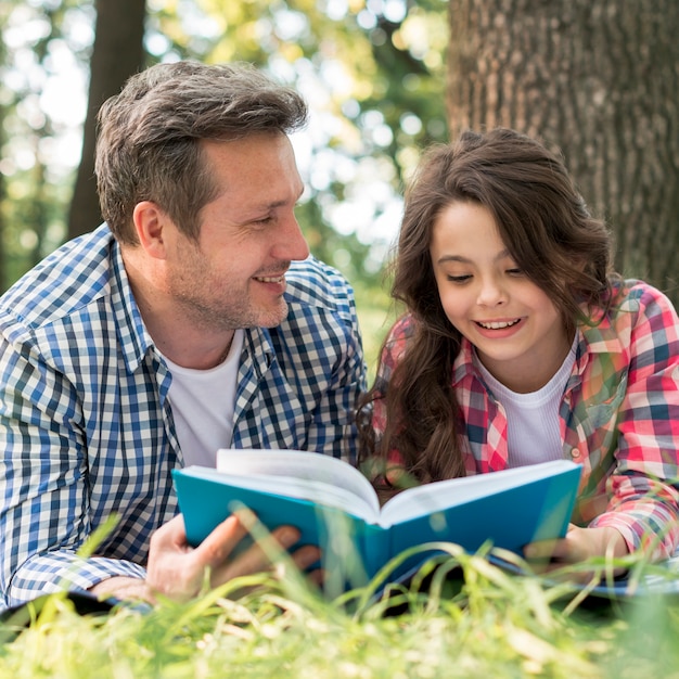 Generi l'esame della sua figlia mentre leggono il libro in parco