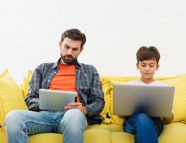 Father looking on tablet and son working on laptop