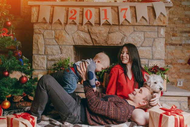 Father lying on the floor with a fireplace in the background while raising his baby up and the mother looks at them smiling