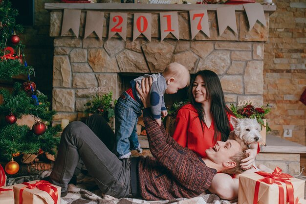 Father lying on the floor with a fireplace in the background while raising his baby up and the mother looks at them smiling