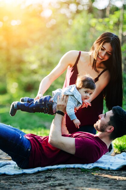 Father lying in a park with his baby up and his mother helping him