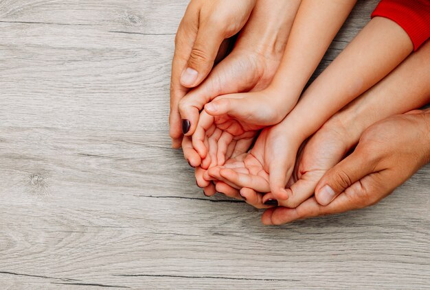 Father, mother and daughter holding hands on top of each other on a light wooden