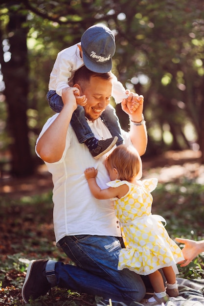 Father plays with his son and daughter on green lawn in park 