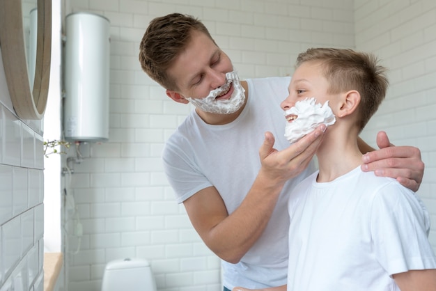 Отец наносит крем для бритья на лицо сына