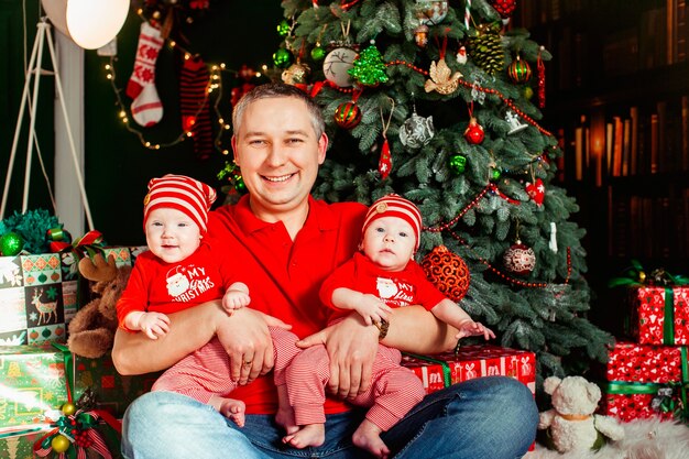 아버지는 크리스마스 트리 전에 빨간 옷에 쌍둥이와 함께 앉아