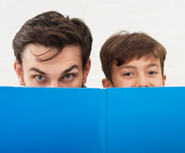 Father and son covering their faces with a blue book