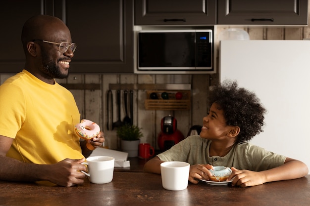 Отец и сын вместе едят пончики на кухне