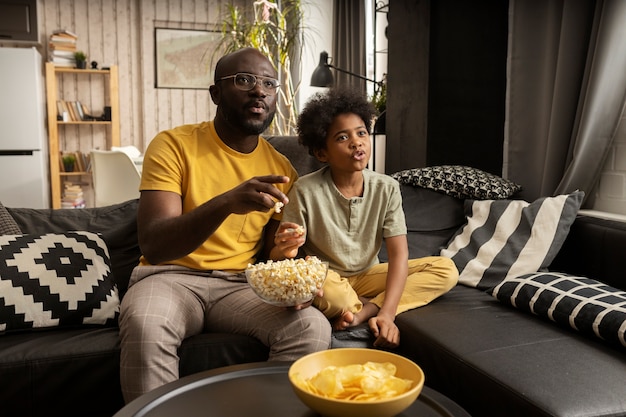 Padre e figlio mangiano popcorn e patatine insieme sul divano