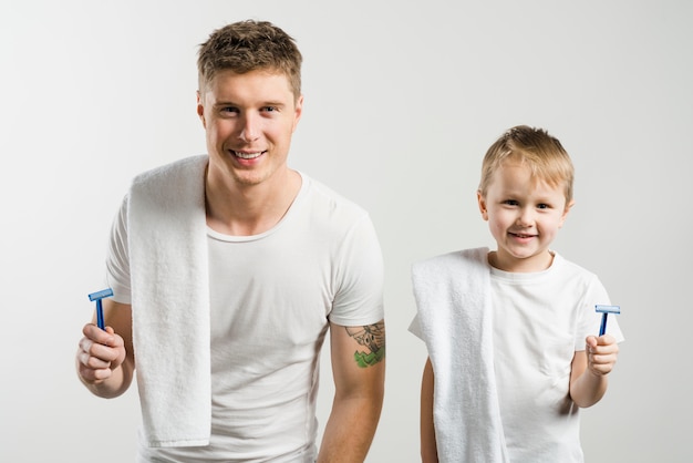 父と息子の白い背景に対してカメラを探して肩越しに白いタオルで手にかみそりを
