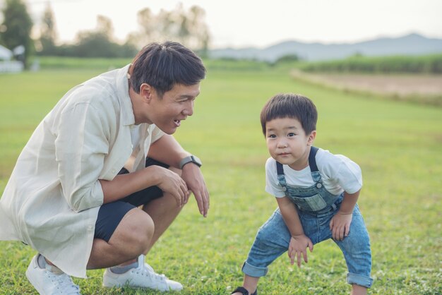 아버지와 아들이 일몰 시간에 공원에서 연주. 사람들은 현장에서 재미. 친절한 가족과 여름 휴가의 개념. 아버지와 아들 다리 공원에서 잔디밭을 가로 질러 걸어