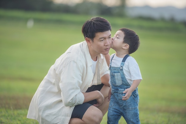 夕暮れ時に公園で遊ぶ父子。フィールドで楽しむ人々。フレンドリーな家族と夏休みのコンセプト。父と息子の足が公園の芝生の上を歩く